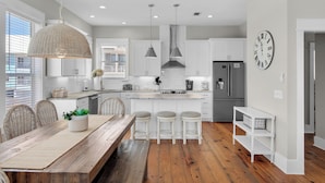 Una cocina moderna con armarios blancos, una isla central con taburetes, una lámpara colgante y un reloj en la pared.