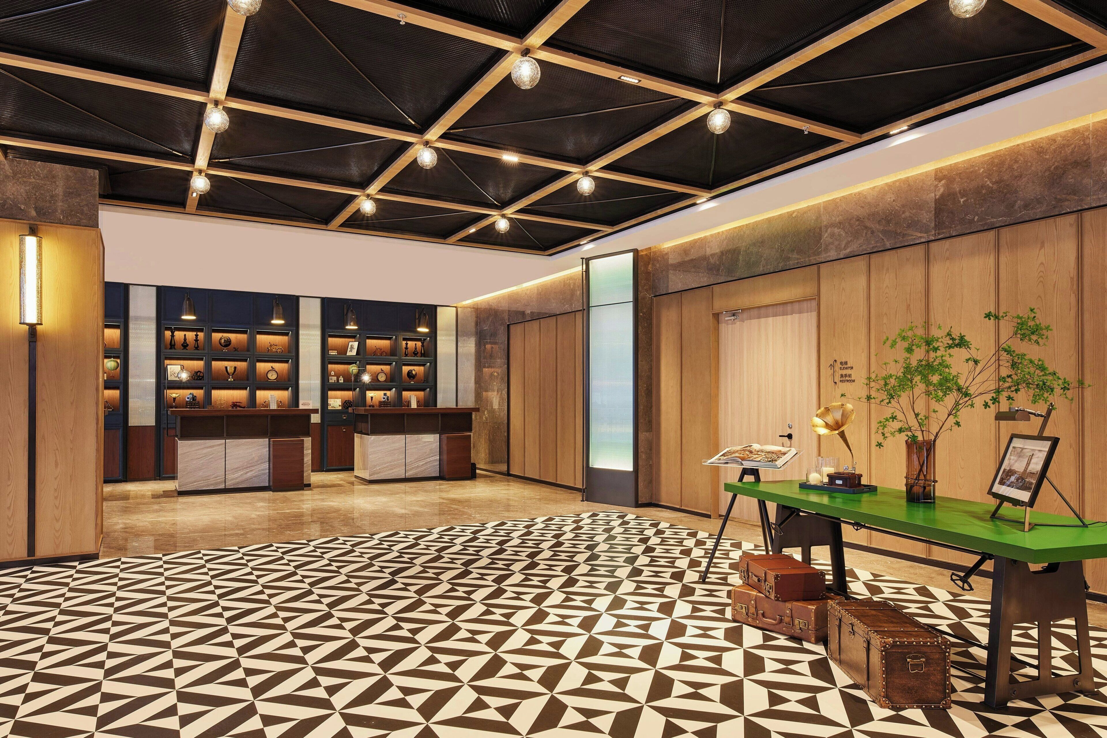 A spacious lobby with a geometric patterned floor, a reception desk, and a wooden panel wall.