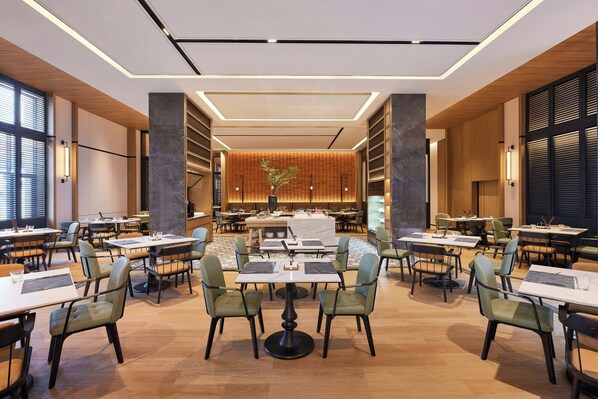A spacious dining area with multiple tables and chairs, a central decorative plant, and a modern ceiling design. - Four Points By Sheraton Kunming Dongfeng Square (Kunming)