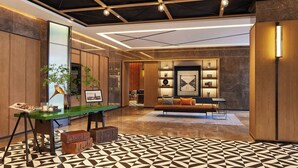 A modern lobby with a geometric patterned floor, a green desk with a lamp, a sofa, and a wall with framed pictures and a shelf with decorative items. - Four Points By Sheraton Kunming Dongfeng Square (Kunming)