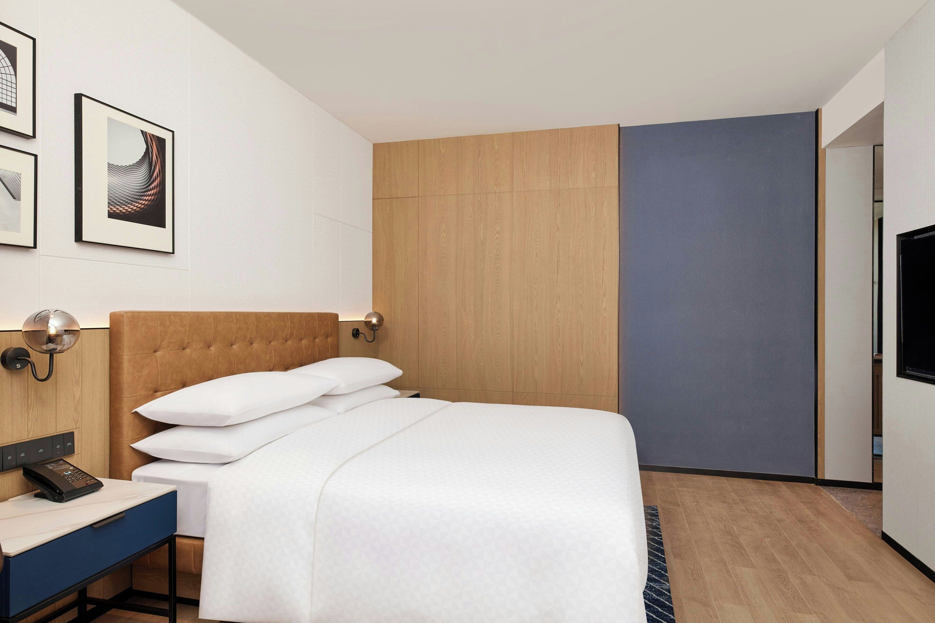 Ein modernes Hotelzimmer mit einem großen Bett, einem Nachttisch mit Telefon, einer Wandleuchte und gerahmten Kunstwerken.