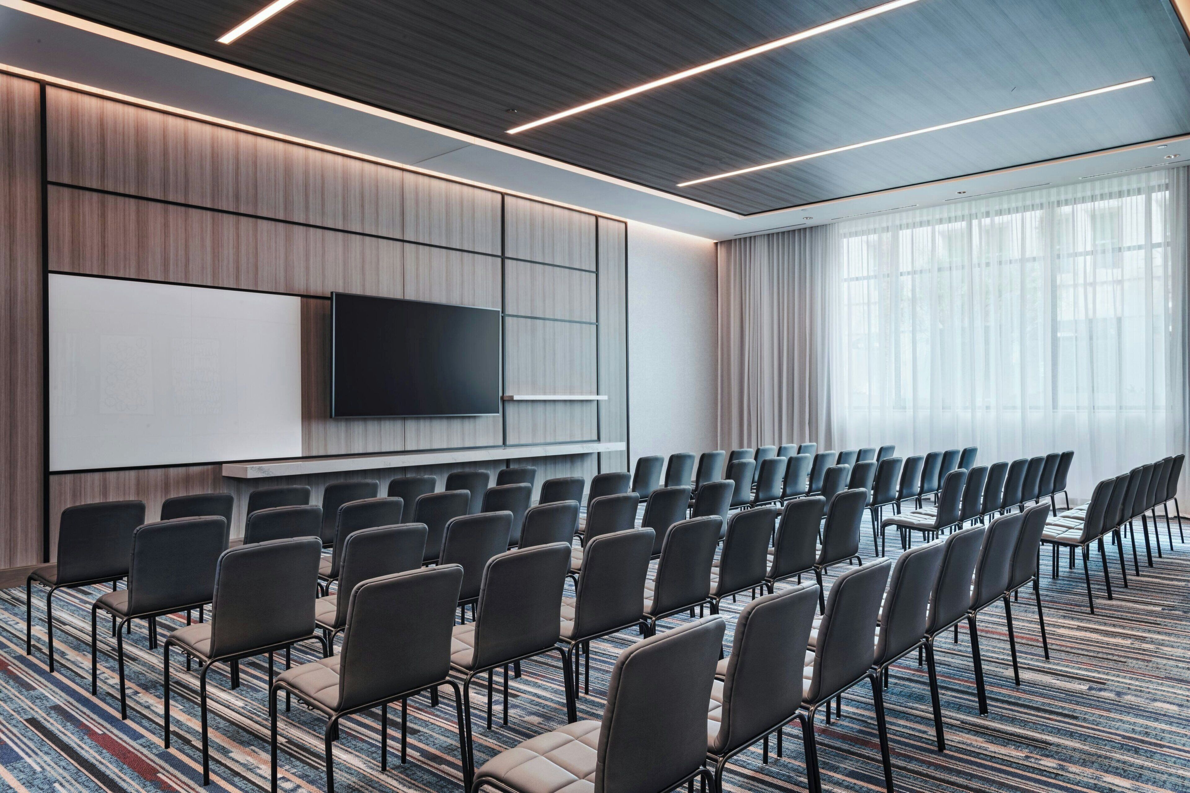 Un salón de conferencias con filas de sillas, un televisor de pantalla plana grande y piso alfombrado.