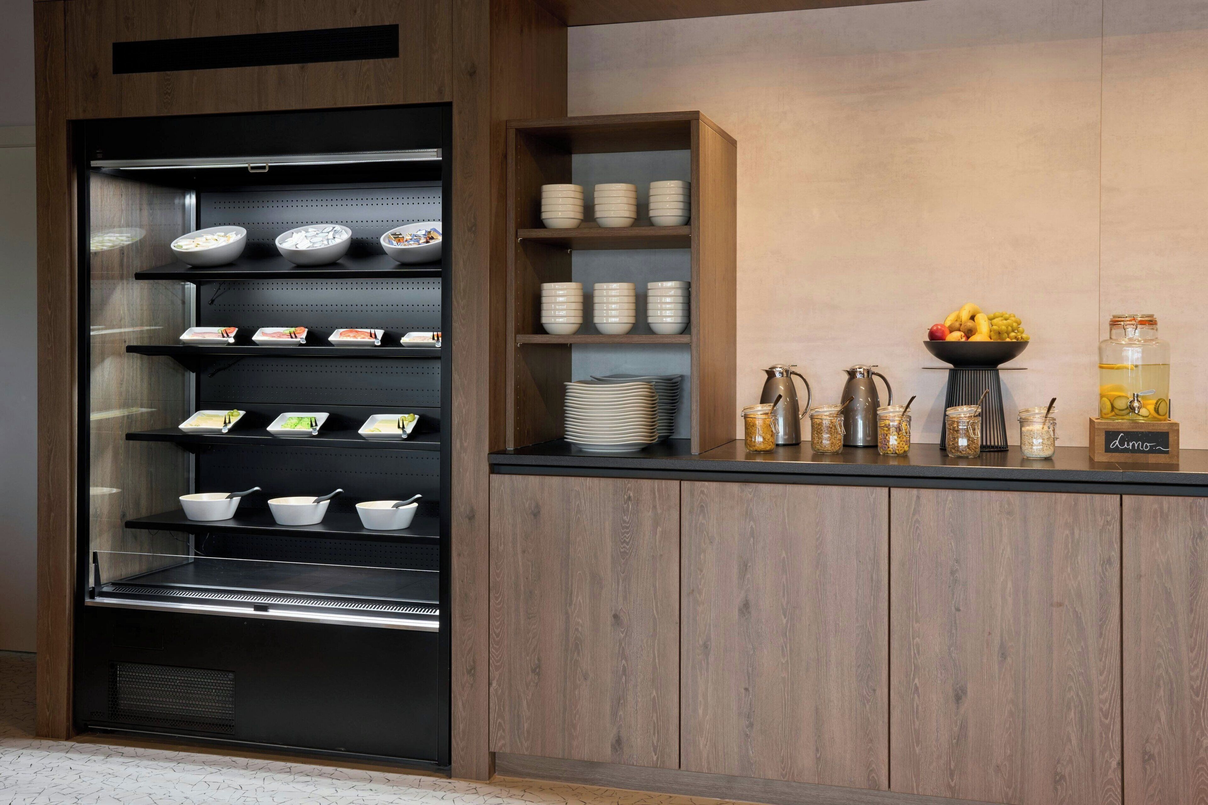 A modern kitchen with a built-in refrigerator, shelves with bowls and plates, a coffee station, and a fruit bowl.