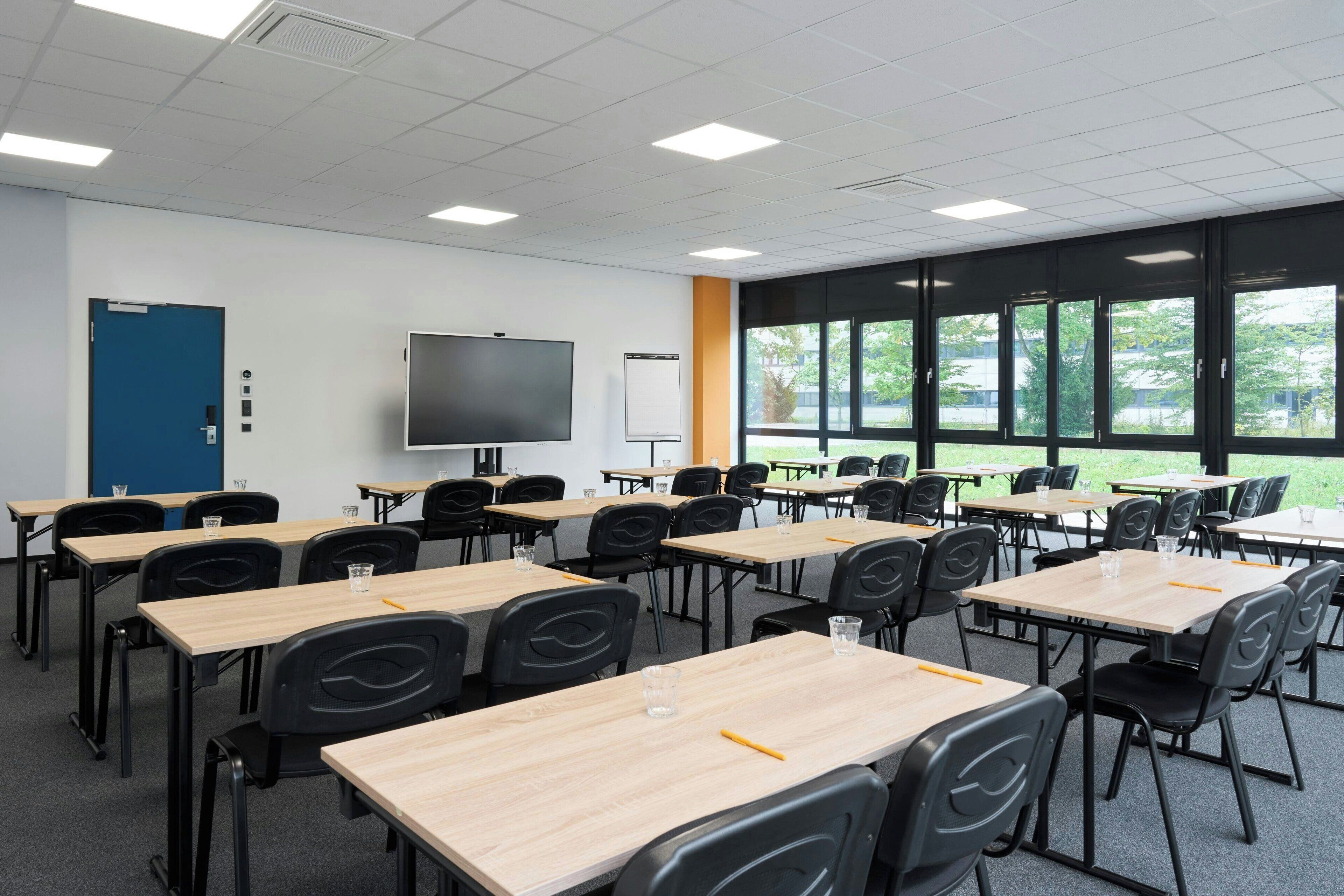 A classroom with desks and chairs arranged in rows, a large screen, and a whiteboard.