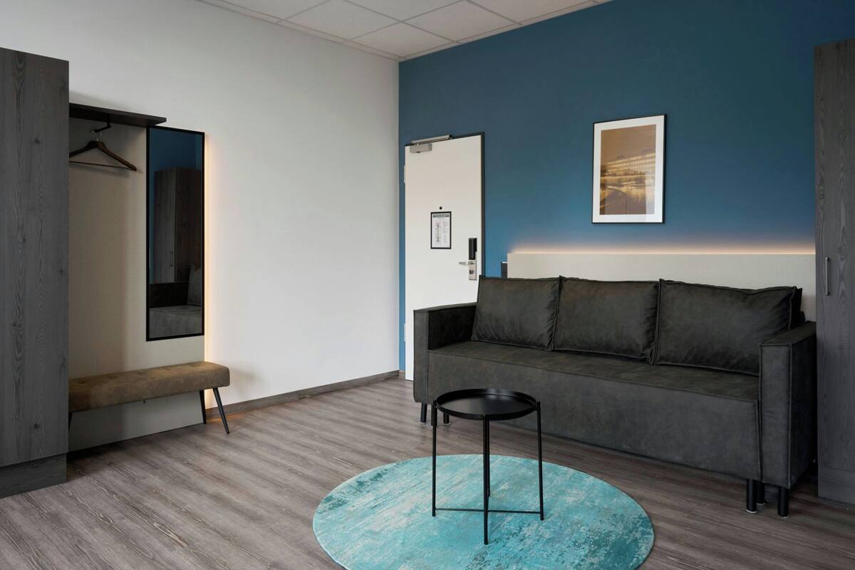 Ein modernes Zimmer mit einem grauen Sofa, einem runden schwarzen Tisch und einem blauen Teppich.