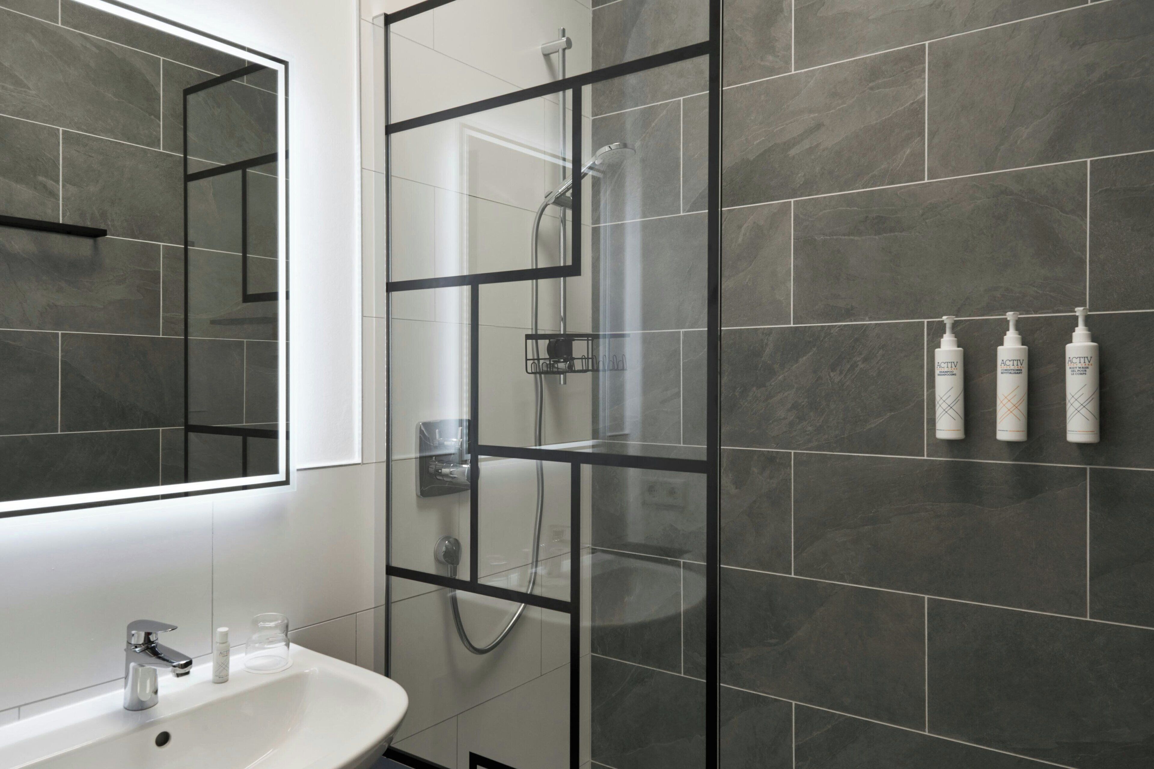 A modern bathroom with a glass-enclosed shower, a white sink, and a mirror.