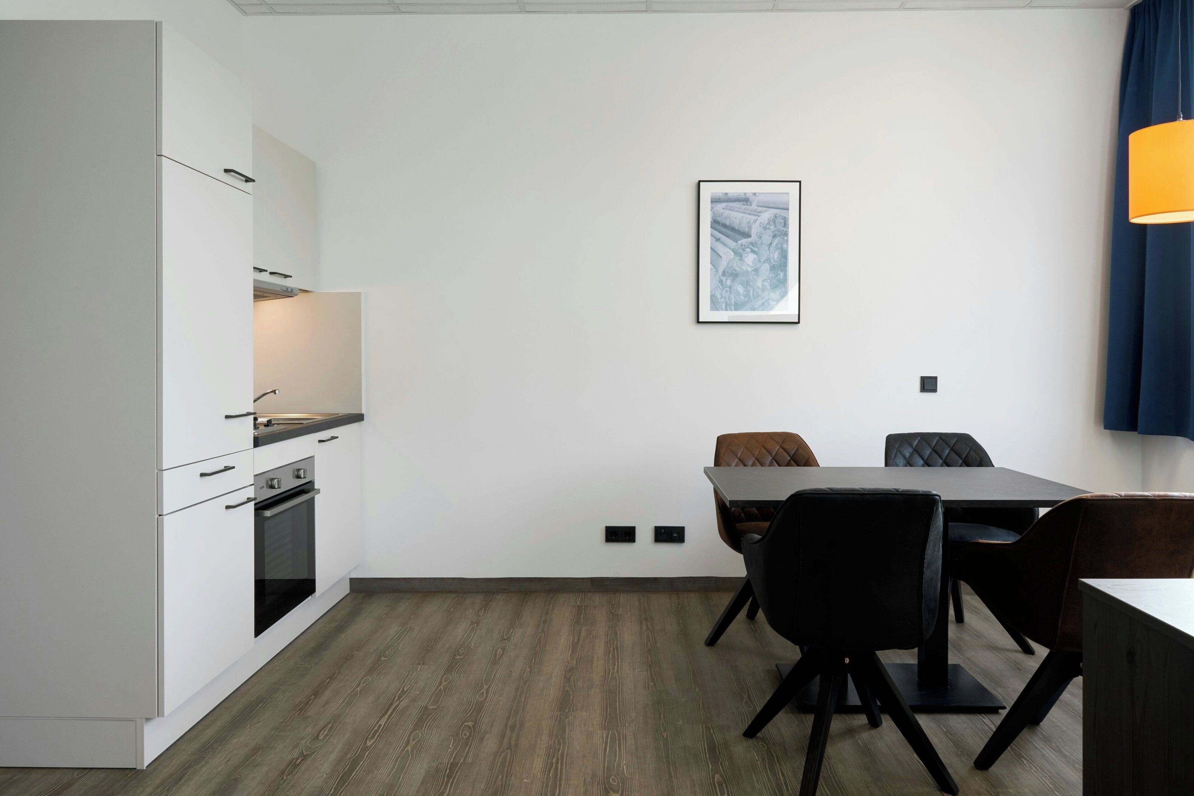 Eine moderne Küche mit weißen Schränken, einem eingebauten Backofen und einem Essbereich mit Tisch und Stühlen.