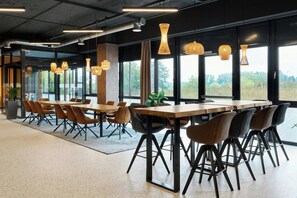 Un comedor moderno con mesas largas y sillas, ventanas amplias y lámparas colgantes.