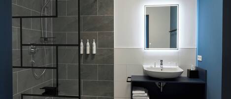 A modern bathroom with a glass shower enclosure, a white sink, and a mirror with integrated lighting.