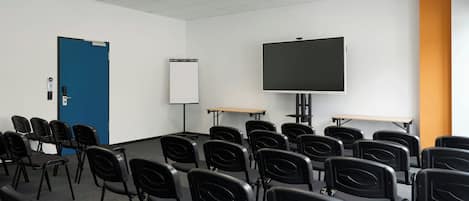 Un salón de conferencias con filas de sillas negras, una pizarra, un proyector y una pantalla grande.