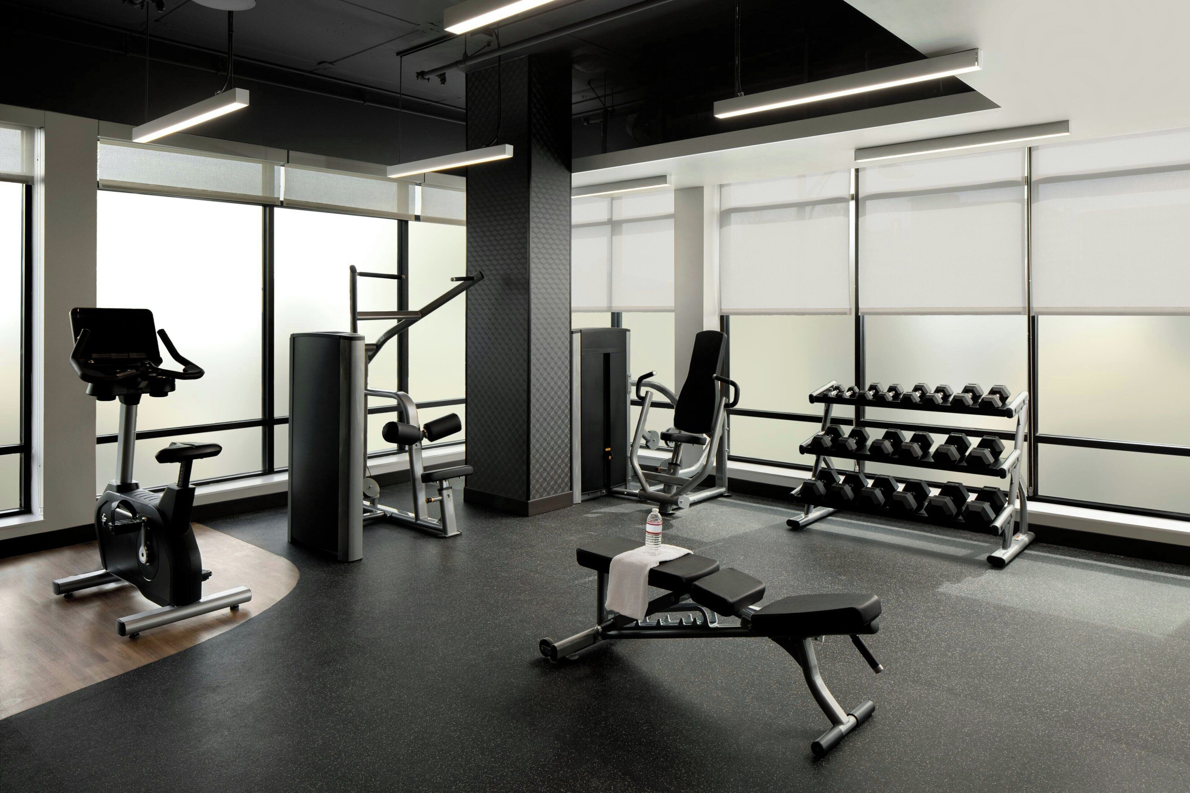Un gimnasio moderno con diversos equipos de ejercicio, amplias ventanas y un interior limpio y bien iluminado.