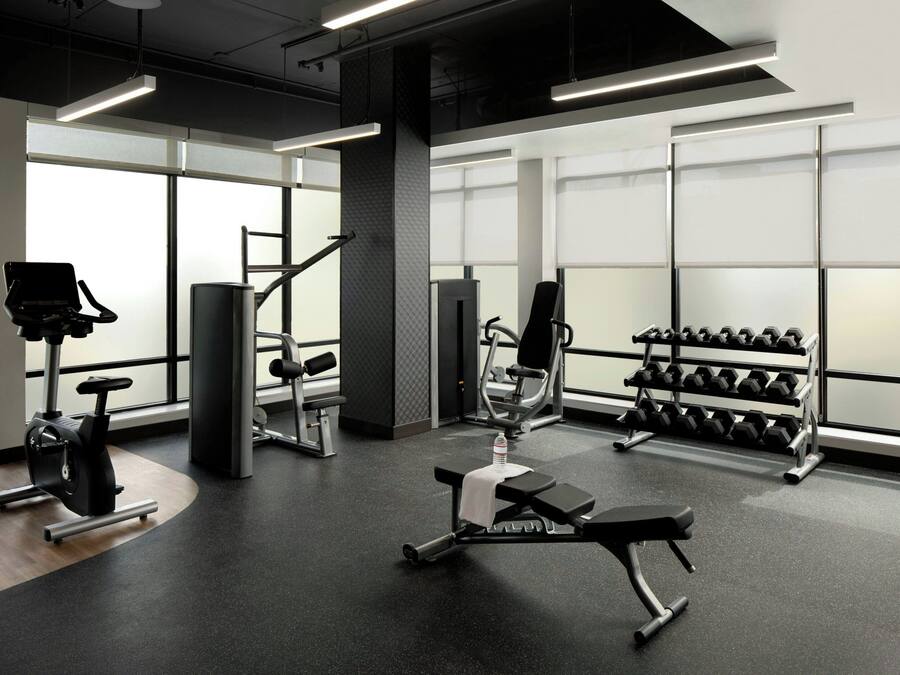 Un gimnasio moderno con diversos equipos de ejercicio, amplias ventanas y un interior limpio y bien iluminado.