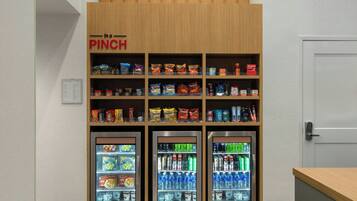 A snack and beverage vending area with multiple shelves stocked with various snacks and drinks, and three refrigerated beverage dispensers.