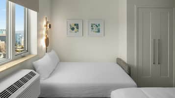 Une chambre d’hôtel avec un grand lit, une fenêtre donnant sur la ville, un climatiseur fixé au mur et deux œuvres d’art encadrées.