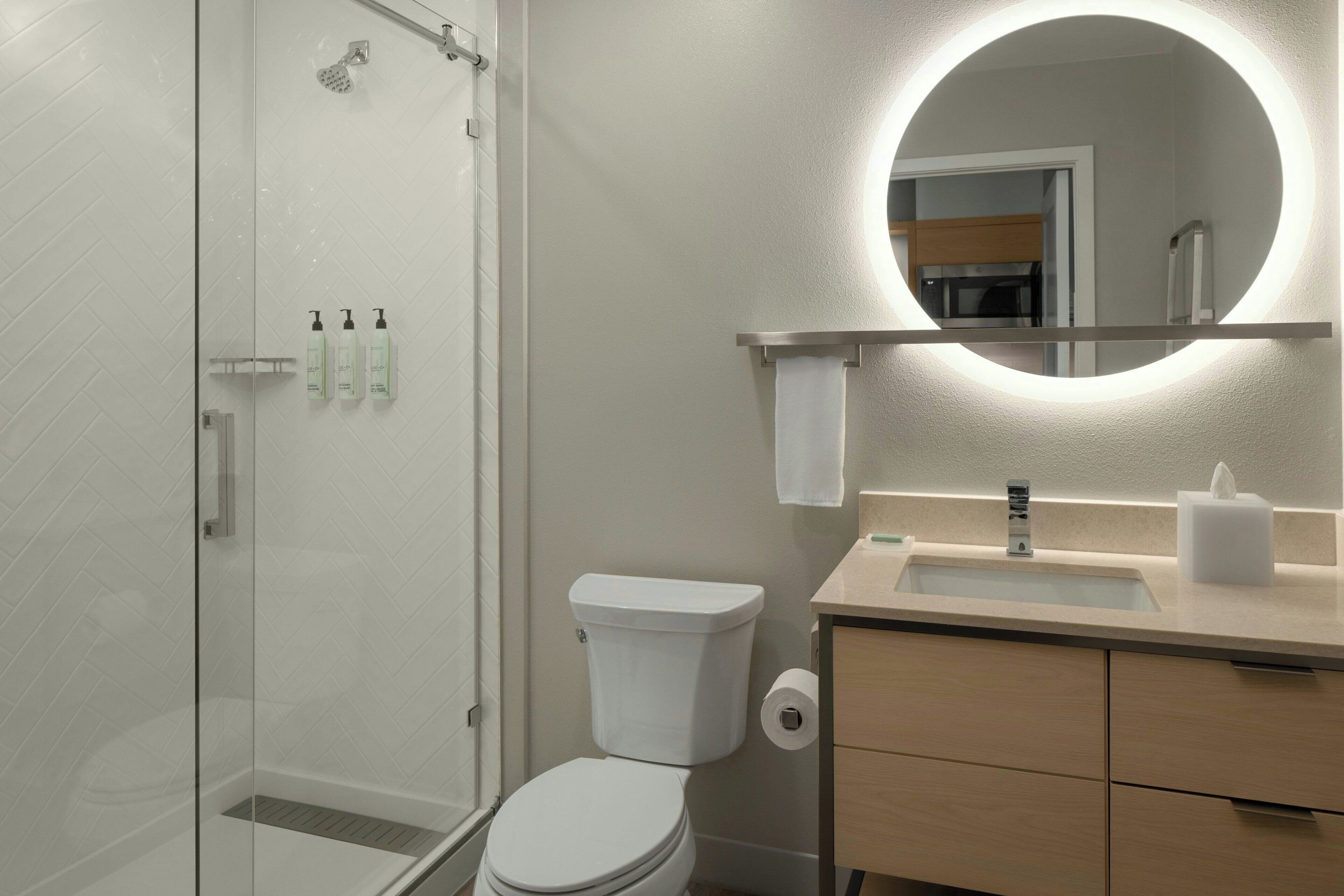 A modern bathroom with a glass shower enclosure, a toilet, a sink with a mirror, and toiletries on the wall.