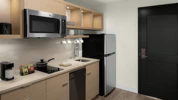 A modern kitchen with a microwave, stove, sink, and dishwasher. There are cabinets above the counter and a black refrigerator.