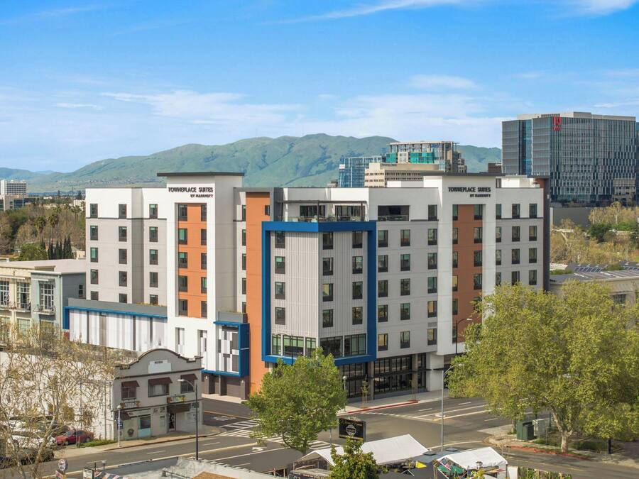 Un hotel de diseño moderno, con una fachada destacada en azul y naranja, rodeado por un paisaje urbano y montañas al fondo.
