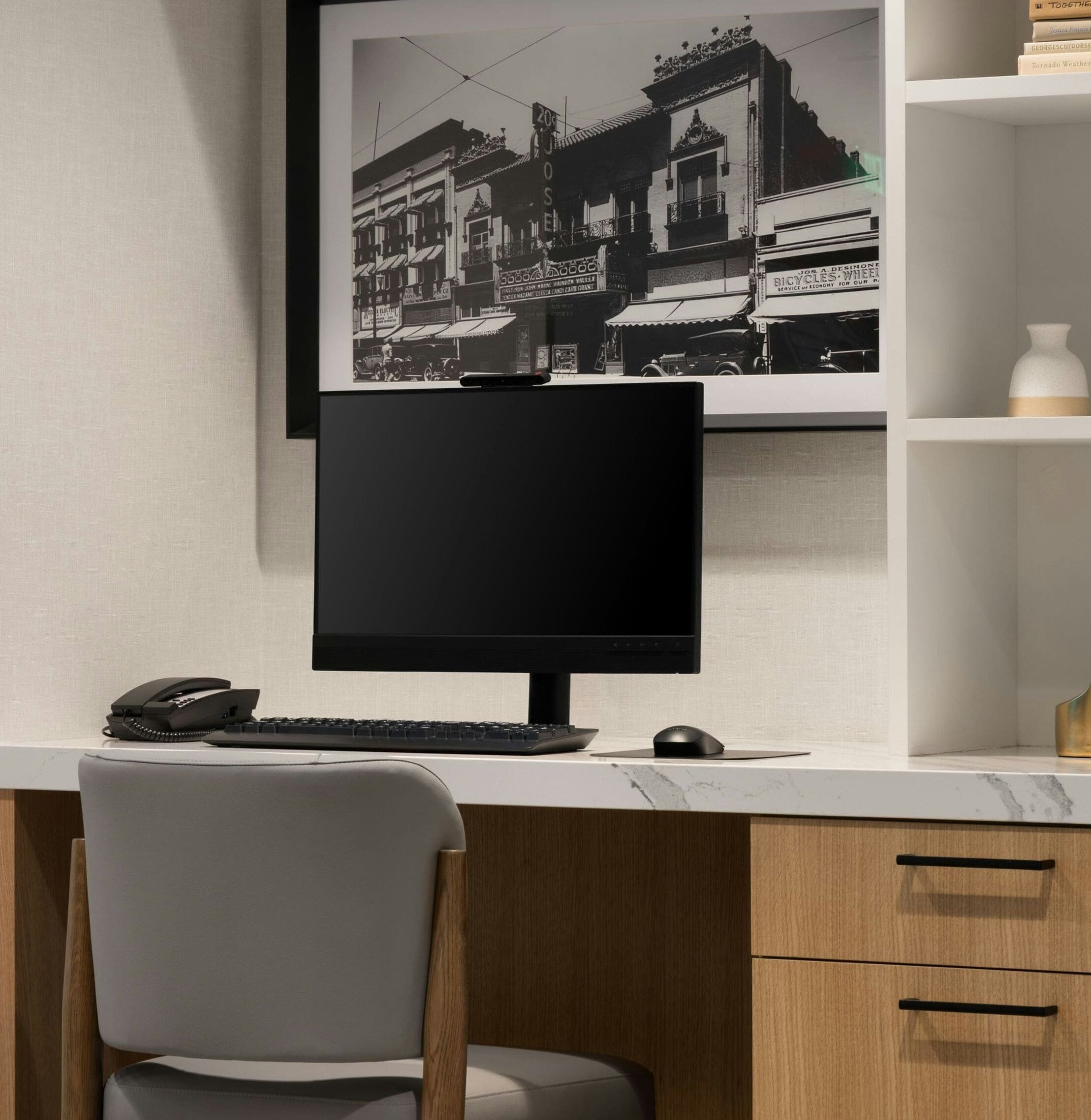 Un escritorio moderno con un monitor de computadora, teclado y ratón. En la pared, una fotografía en blanco y negro enmarcada de una escena callejera.