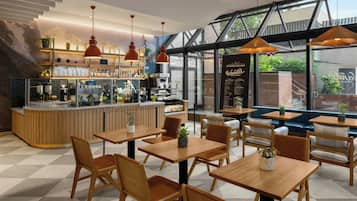 A modern cafe with wooden tables and chairs, a bar area, and large windows offering views of the outdoors.