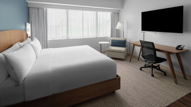 A hotel room with a large bed, a desk with a chair, a TV, and a window with curtains.