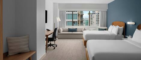 A hotel room with two beds, a sofa, a desk, and a chair.
