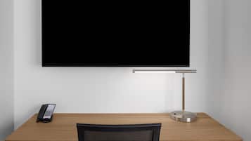 A modern office desk with a flat-screen TV, a desk lamp, and a telephone.