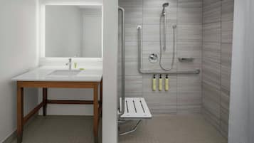 Un baño con tocador de madera, un espejo, ducha con cabezal de ducha manual y barra de apoyo.