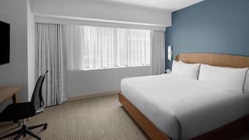 Habitación de hotel con una cama grande, un escritorio, una silla y un ventanal con cortinas.