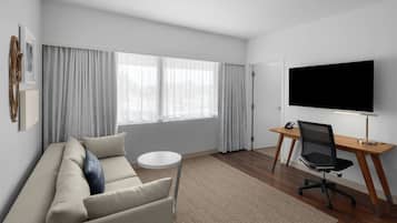 A modern living room with a sofa, a round coffee table, a TV, and a desk with a chair.