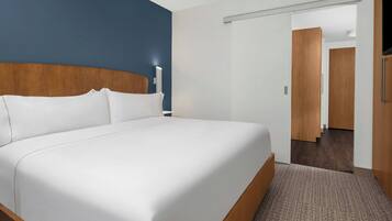 A hotel room with a large bed, a wooden headboard, a white wall, and a door leading to another room.