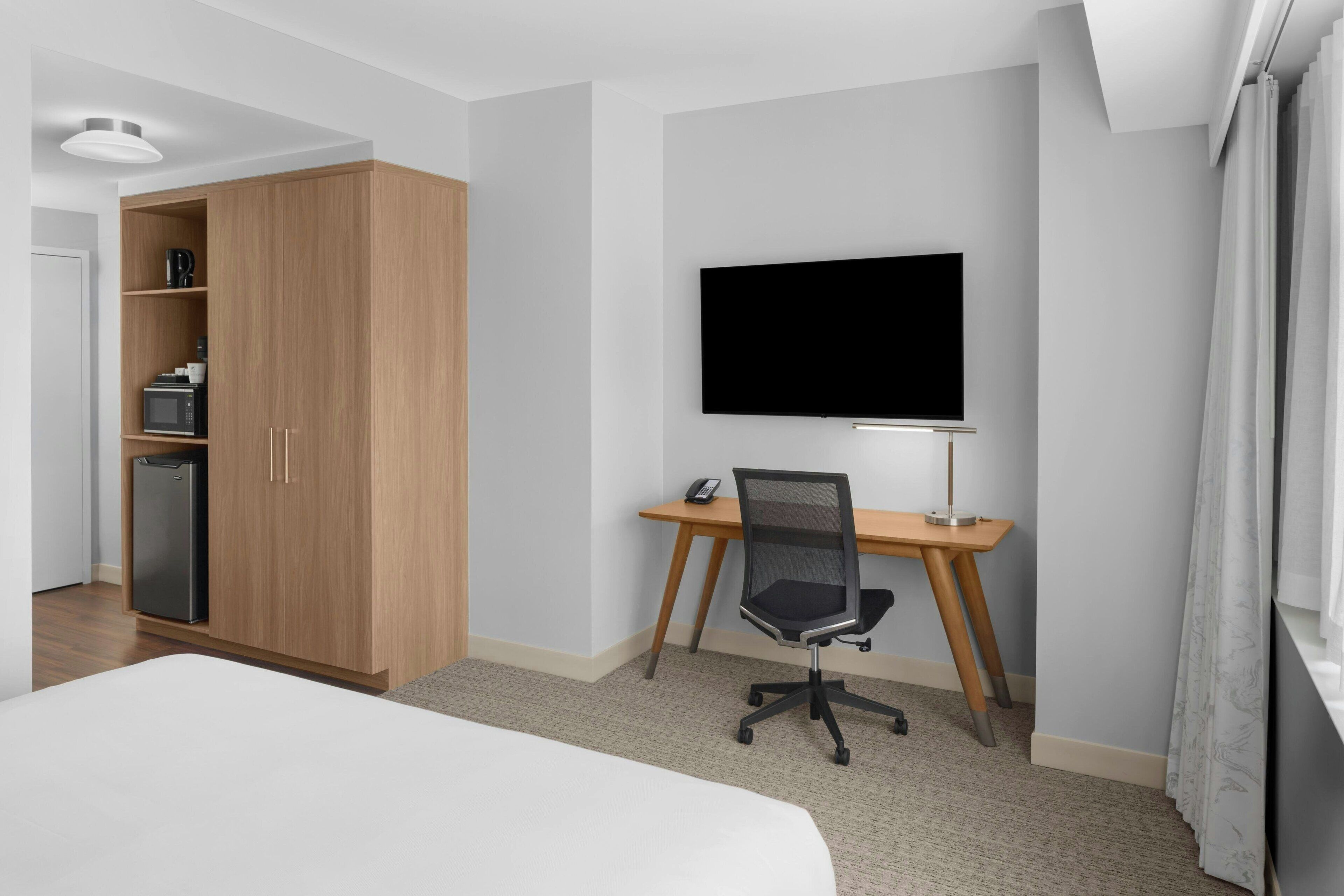 A hotel room with a bed, a desk with a chair, a TV, a wardrobe, and a microwave.