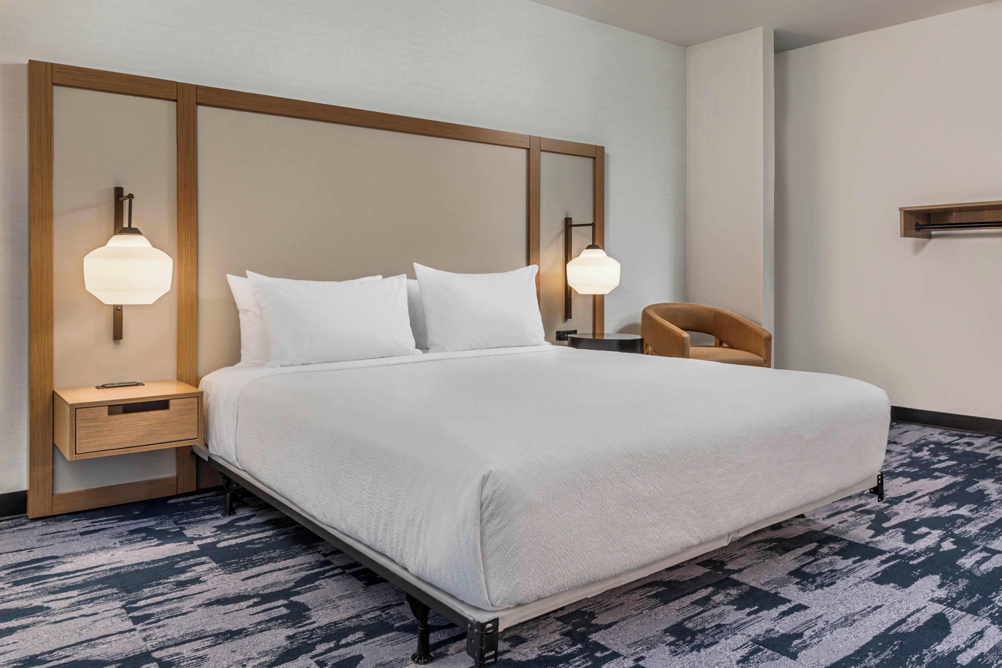 A hotel room with a large bed, two bedside tables, a wooden headboard, and two wall-mounted lamps.
