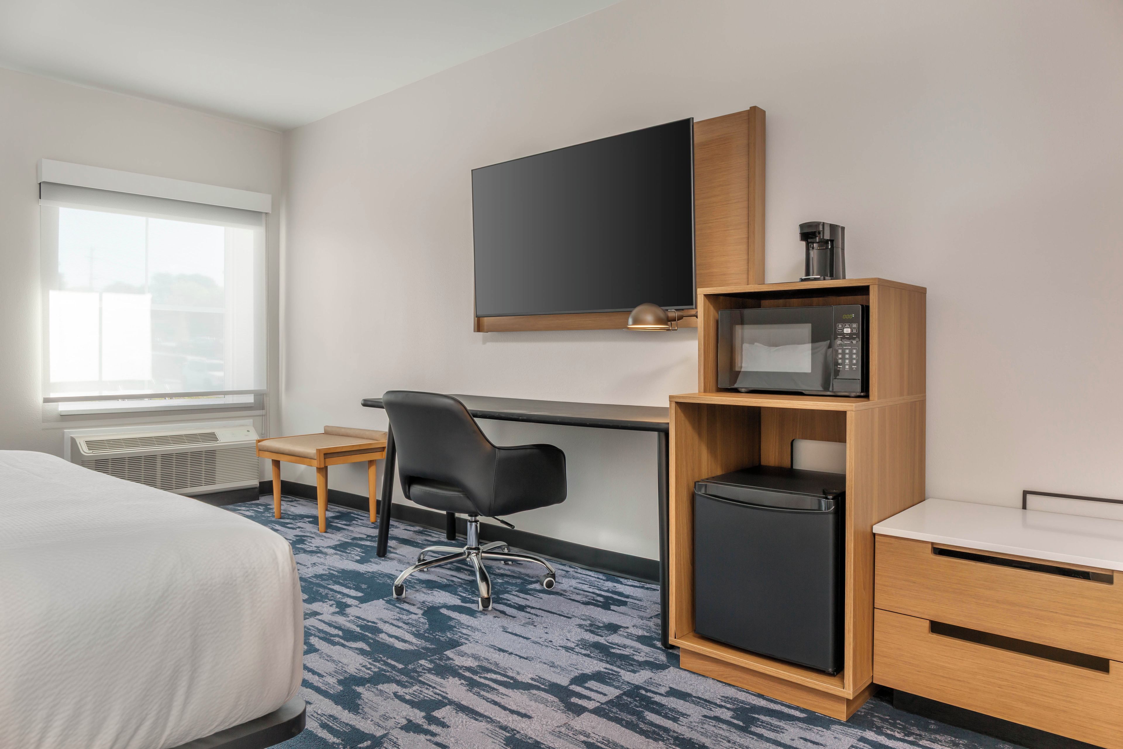 Une chambre d’hôtel équipée d’un lit, d’un bureau, d’une chaise, d’une télévision, d’une machine à café et d’un réfrigérateur.