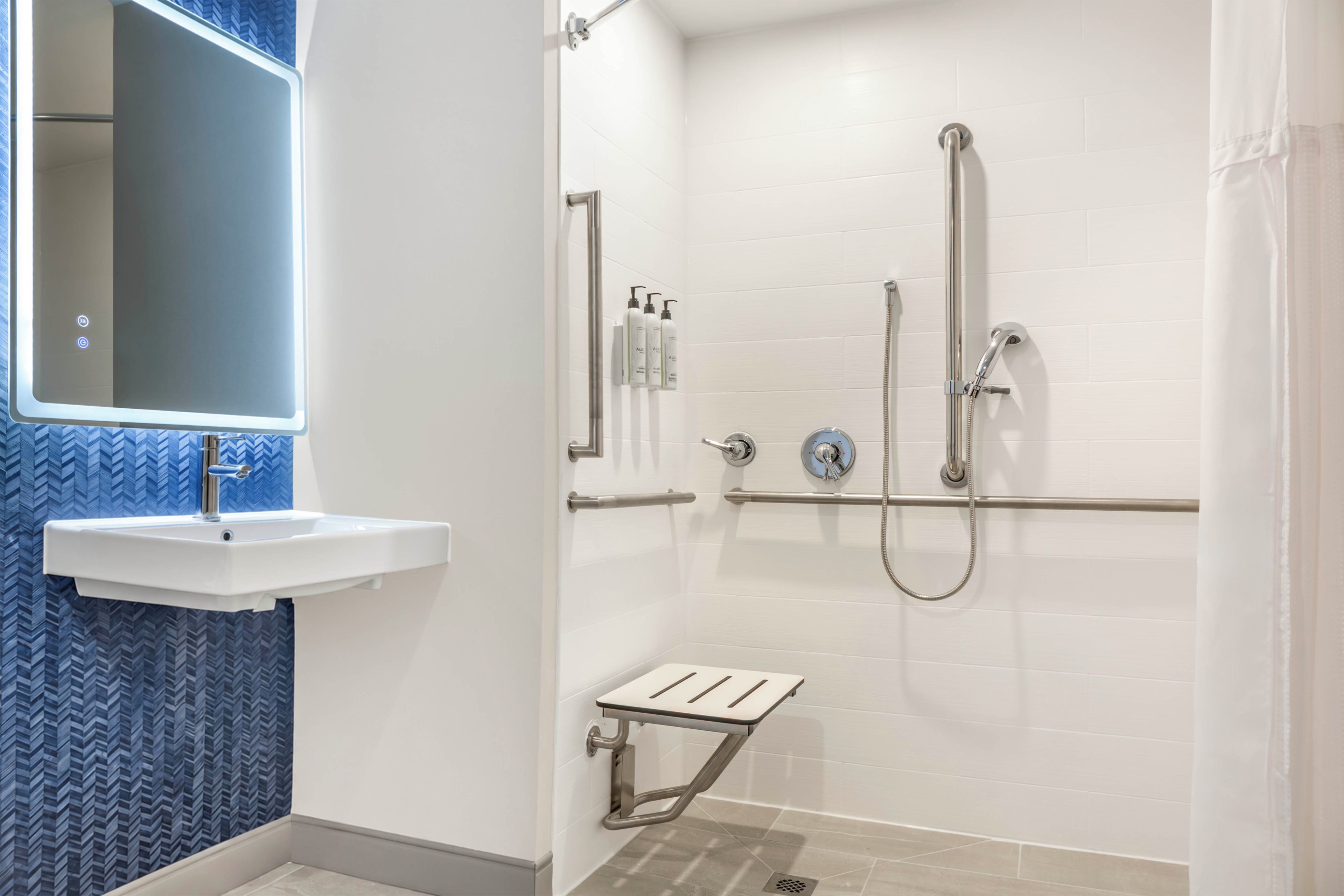 A bathroom with a white sink, a mirror, a shower with a handheld showerhead, and a grab bar.