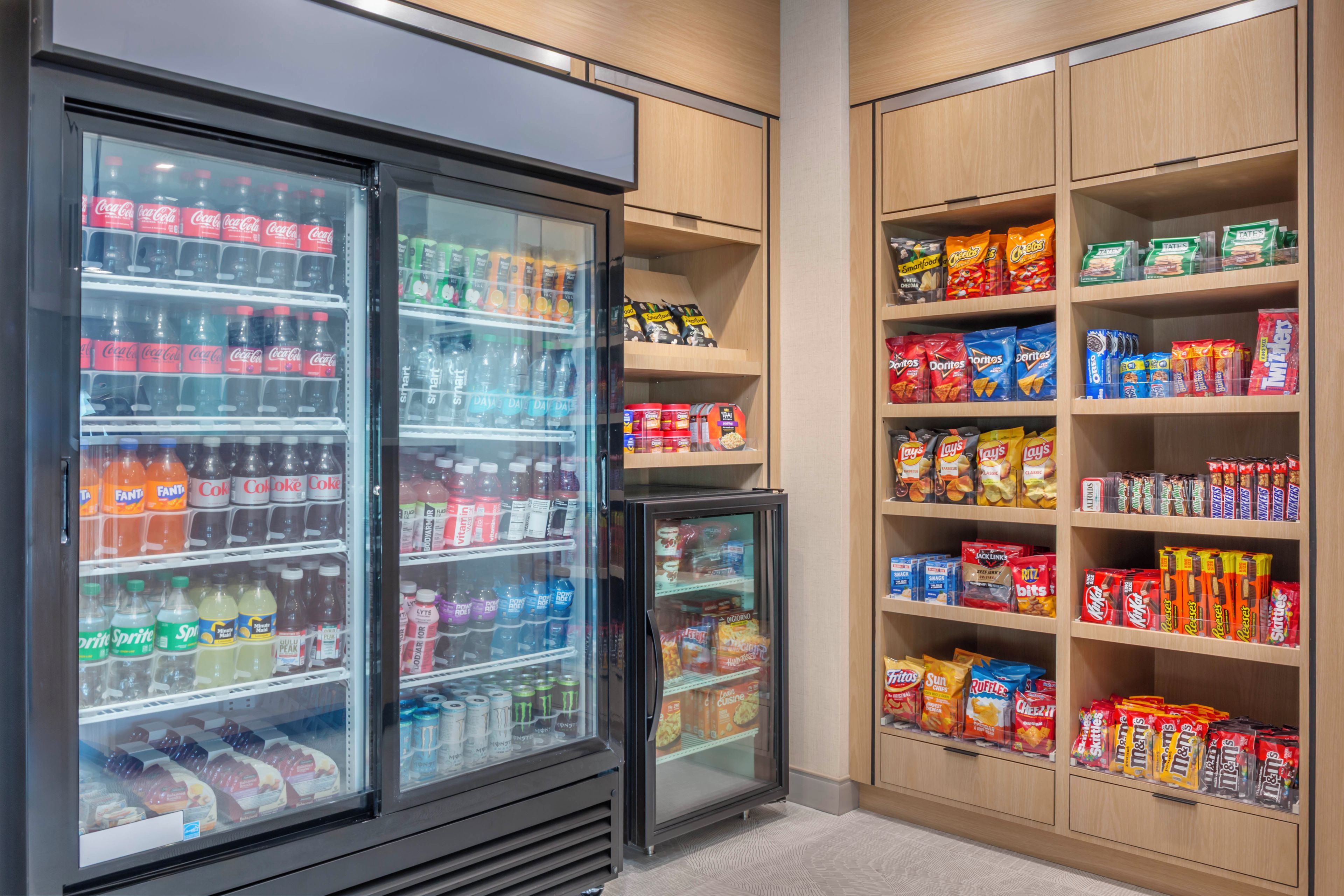A beverage cooler stocked with various drinks and a snack shelf with assorted packaged foods.