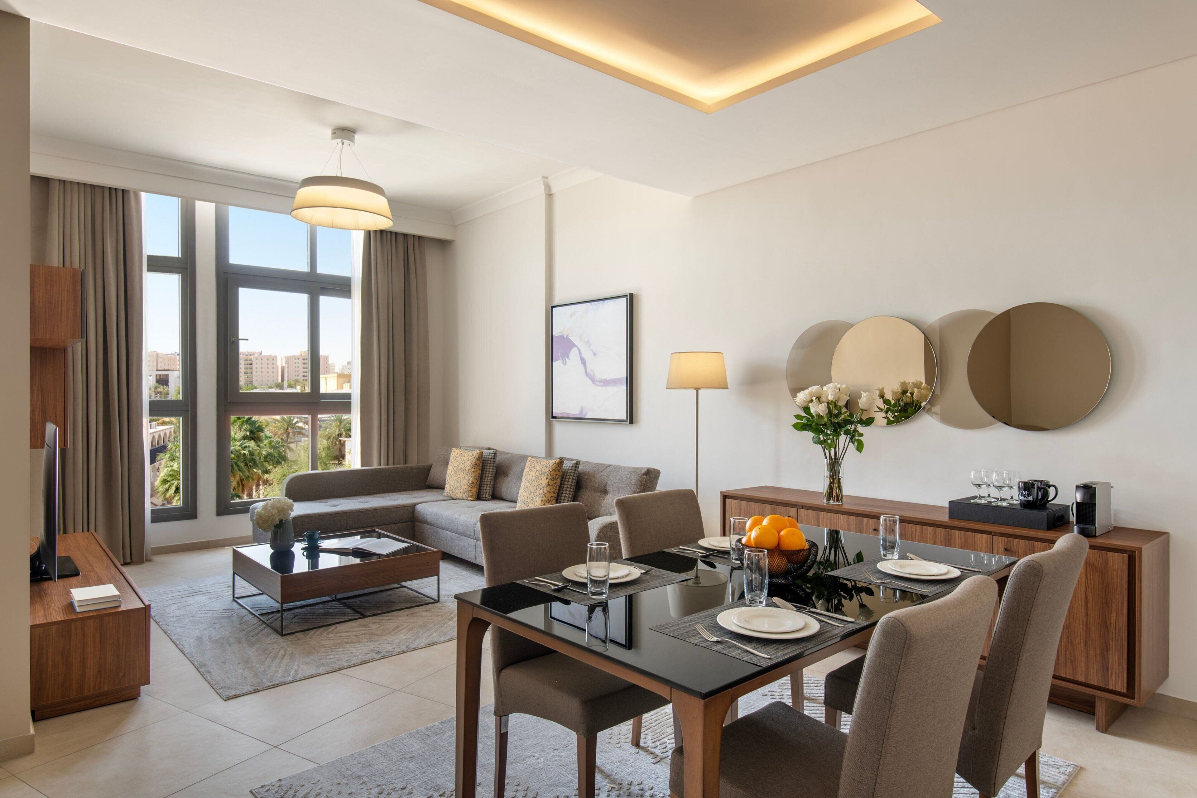 Una habitación de hotel moderna con zona de comedor, sofá y una ventana grande con vistas a la ciudad.