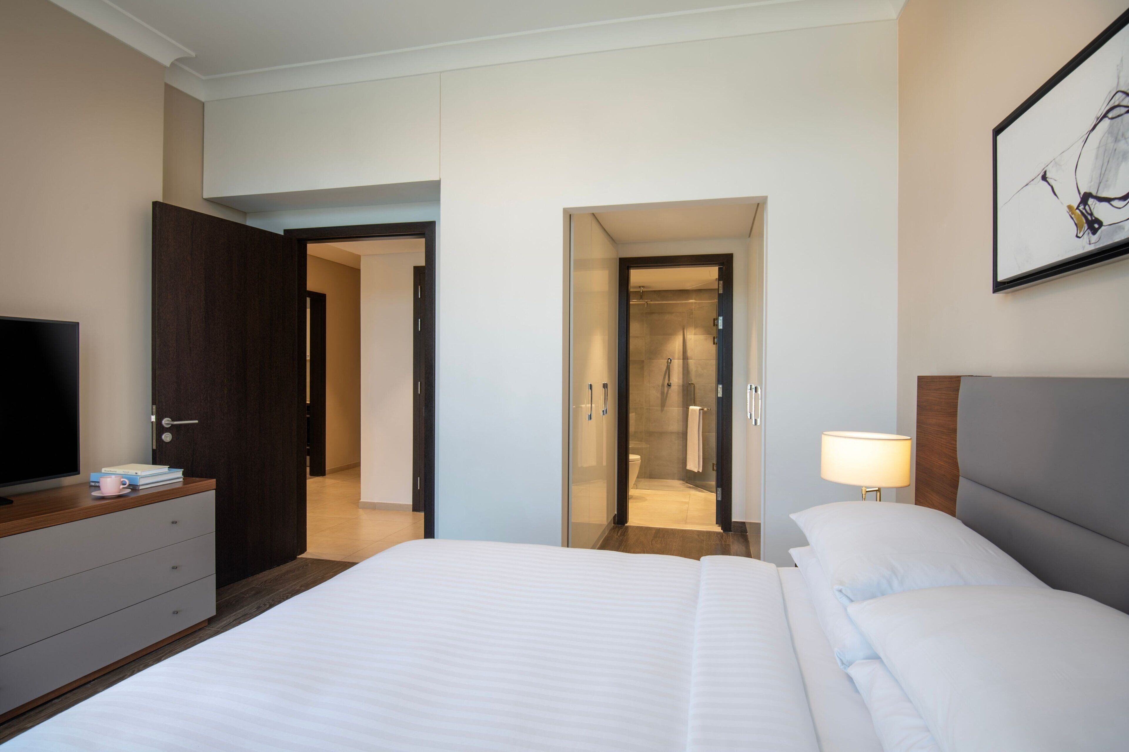 A hotel room with a large bed, a TV on a dresser, a walk-in closet, and a shower area.