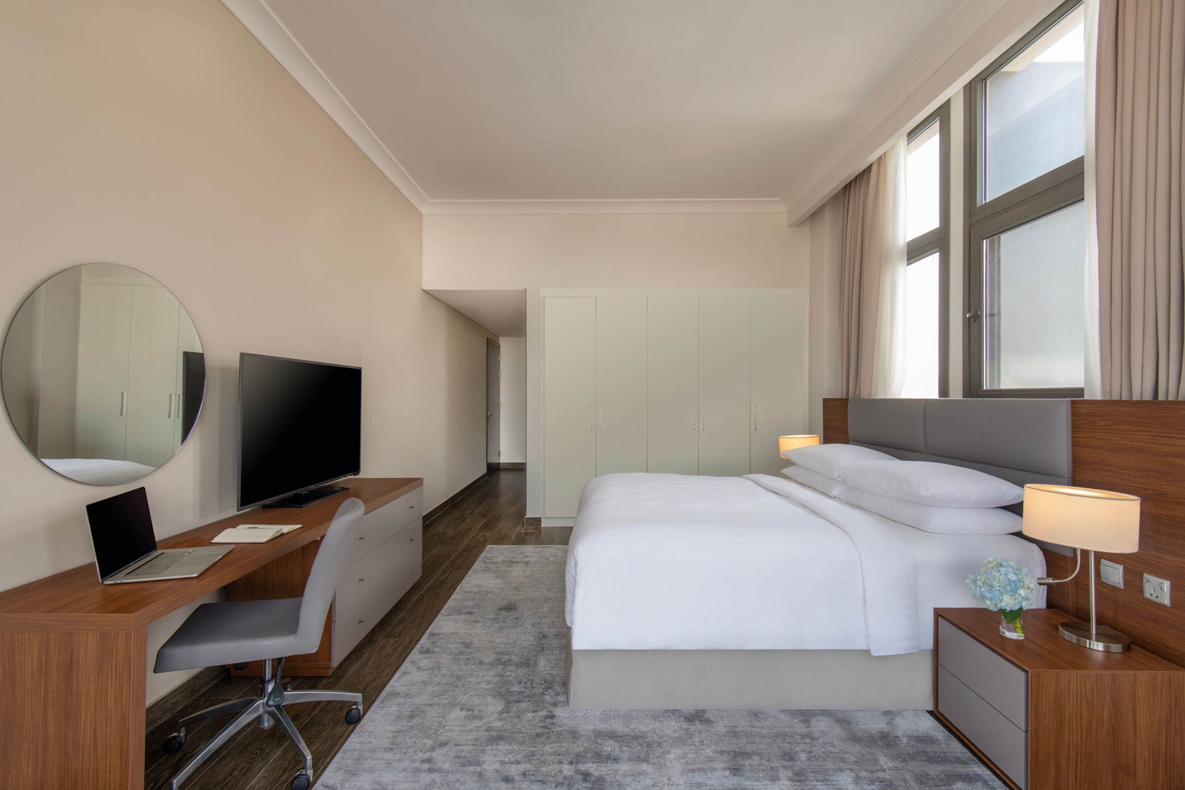 Een hotelkamer met een bed, een bureau met een laptop, een televisie en een spiegel.