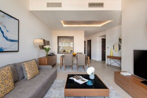 Una sala de estar moderna con un sofá, una mesa de centro y un televisor. Hay una zona de comedor con una mesa y sillas, y una cocina al fondo.