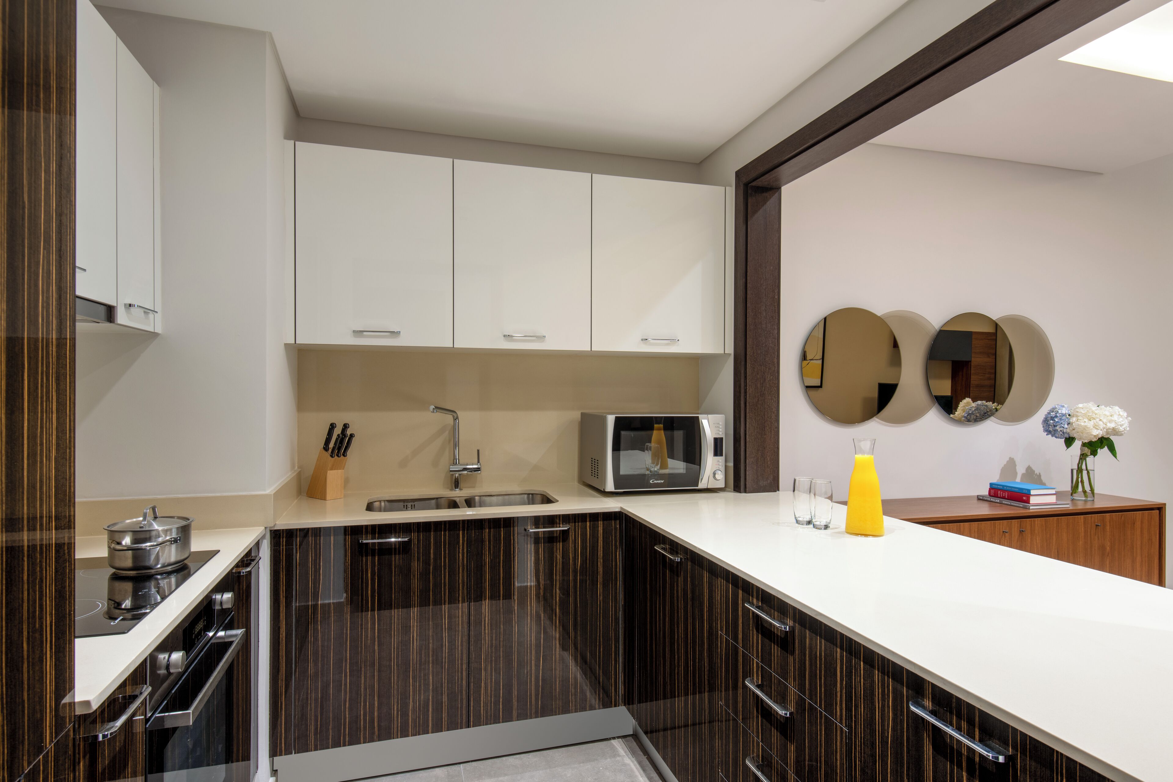 Una cocina moderna con armarios oscuros, un microondas, un lavamanos y una encimera con un vaso de zumo de naranja.