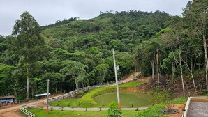 A lush green landscape with a white fence, a small pond, and a hill in the background. - Refúgio da Montanha - Angelina - SC (Angelina)