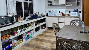 A compact kitchen with white cabinets, a dining table, and a variety of kitchen appliances. - Refúgio da Montanha - Angelina - SC (Angelina)