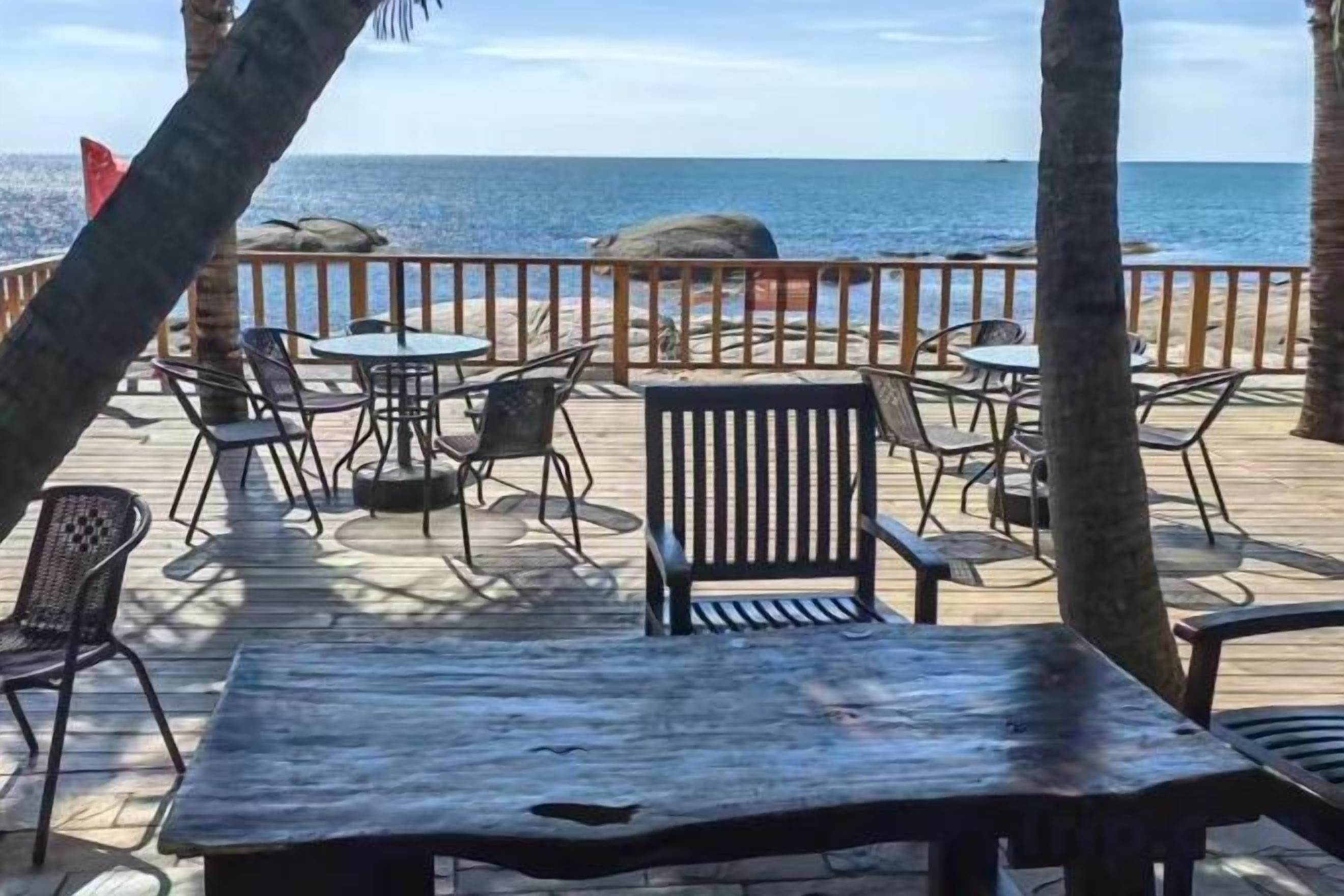 A wooden deck with tables and chairs, overlooking the sea.