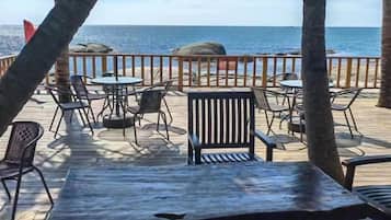 A wooden deck with tables and chairs, overlooking the sea.