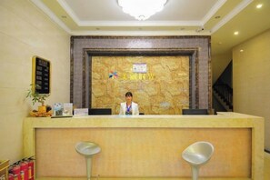 A reception desk with a receptionist, a wall-mounted information board, and two bar stools. - Meili Shiguang Holiday Hotel (Sanya)