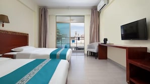 A hotel room with two beds, a TV, a desk, and a view of the city.
