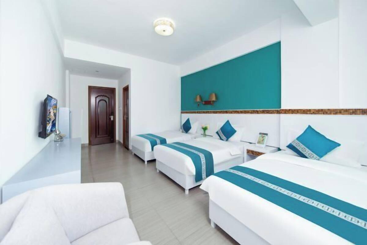 Quarto de hotel com duas camas, um sofá, uma televisão e um banheiro visível ao fundo.