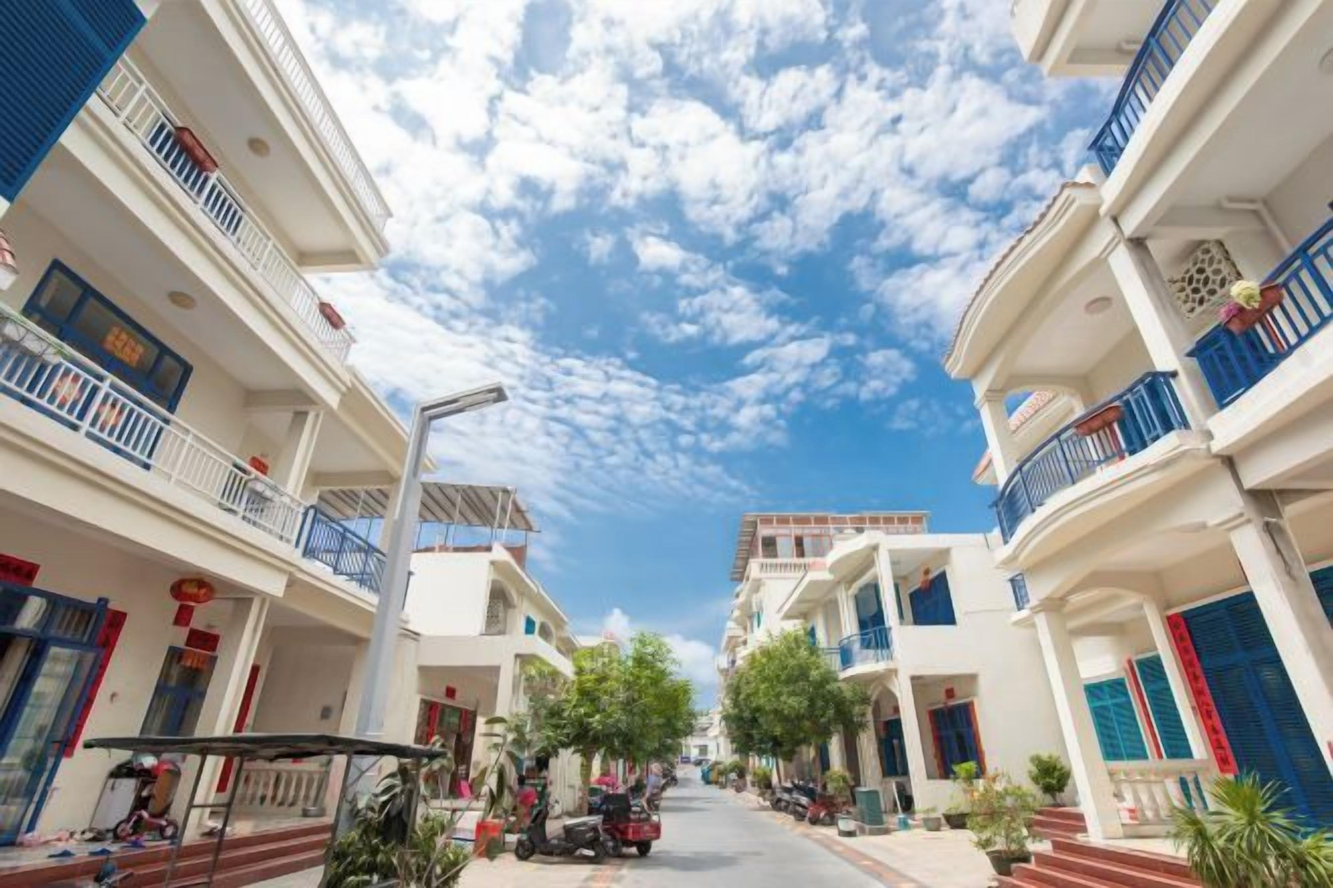 A street view with multi-story buildings, balconies, and a clear sky.