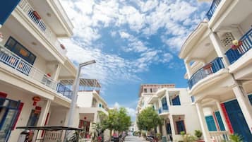 A street view with multi-story buildings, balconies, and a clear sky.