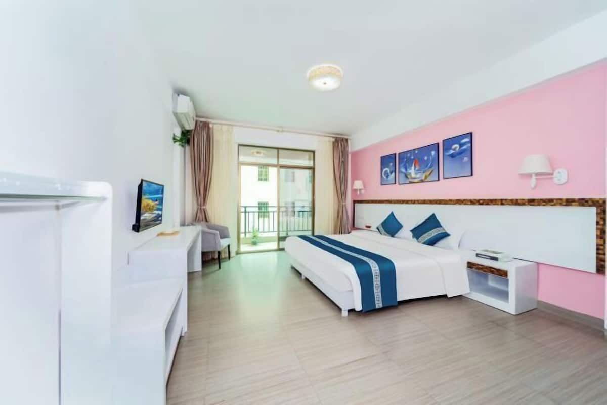 Quarto de hotel com cama, escrivaninha, cadeira, janela com cortinas e parede com quadros.